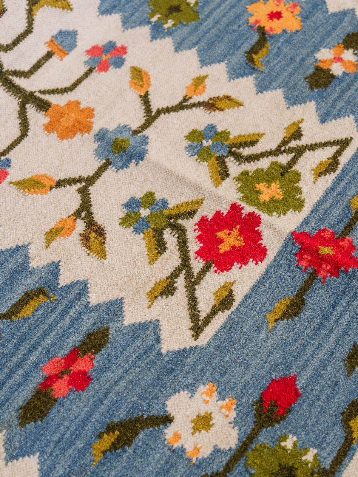 A woven textile with a floral pattern on a blue and off-white background, showing red, blue, orange, yellow, and green details.