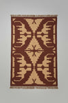 A large woven area rug with a geometric tribal pattern in dark brown and beige.