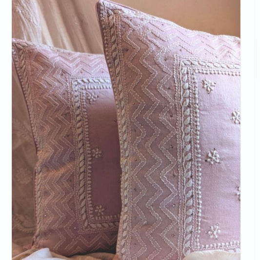 Two dusty pink embroidered cushion cover pillows with white floral and geometric stitching. hand done skilled chikankari made in india,styled on a sofa.
