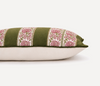 A close-up of a decorative throw pillow featuring olive green velvet fabric with vertical panels of pink and white floral embroidery, resting on a plain off-white surface against a white background.