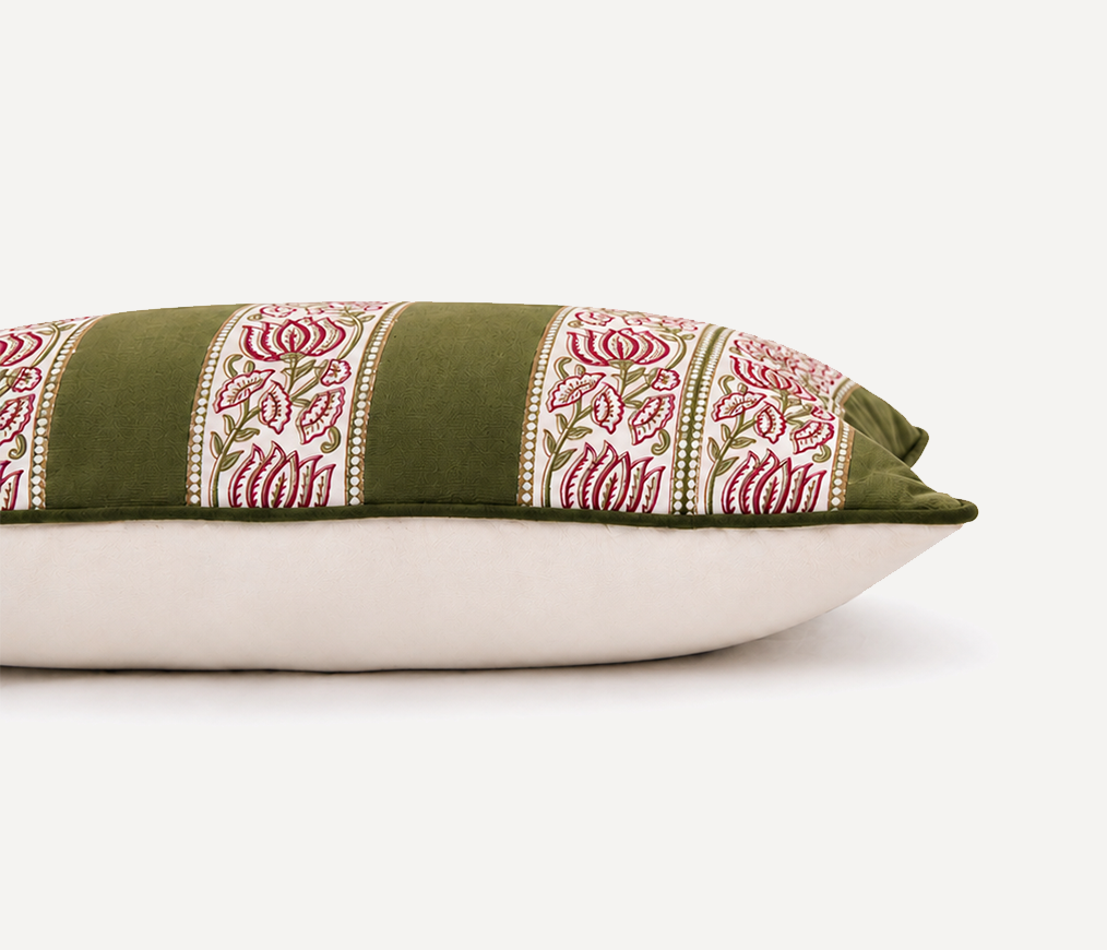 A close-up of a decorative throw pillow featuring olive green velvet fabric with vertical panels of pink and white floral embroidery, resting on a plain off-white surface against a white background.