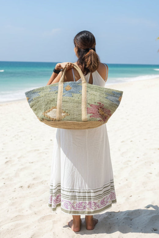 A large woven tote bag with a colorful paisley pattern and beige handles for a beach vacation.