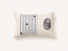 An off-white rectangular lumbar pillow featuring a vertical stripe pattern in blue and gray on the left, three small dark red buttons, and an oval floral motif on the right.