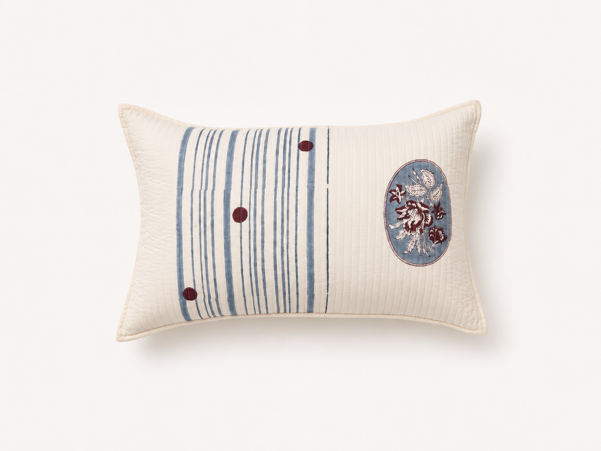 An off-white rectangular lumbar pillow featuring a vertical stripe pattern in blue and gray on the left, three small dark red buttons, and an oval floral motif on the right.