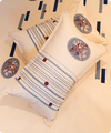 A decorative rectangular throw pillow with blue stripes and embroidered floral medallions, resting on a matching patterned cream bedding set.