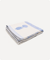 A folded white cotton table linen or napkin with a blue floral print and a blue patterned border, shown on a light off-white background.