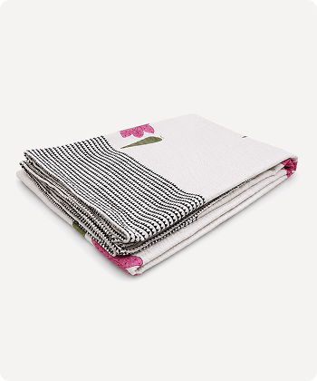 A folded white textile item, likely a blanket or throw, featuring a black and white striped pattern on one side and small pink floral accents with green stems.