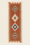 A long rectangular woven runner rug with a Southwestern geometric pattern in terracotta orange, cream, navy blue, and gray, laid out on a gray tiled floor.