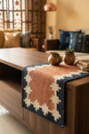 A long rectangular hand woven runner rug . The rug has a terracotta pink center, cream geometric borders, and a black border.
