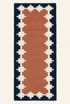 A long rectangular hand woven woolen  runner rug laid flat. The rug has a terracotta pink center, cream geometric borders, and a dark navy outer border.