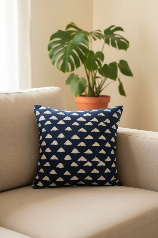 A square throw pillow with a navy blue and white geometric triangle pattern, resting on an orange upholstered armchair in front of patterned wallpaper.