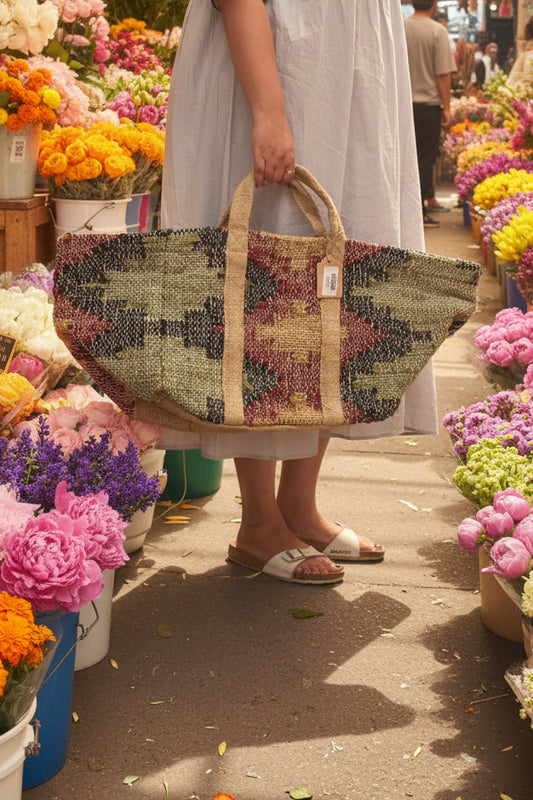 A large woven tote bag with a geometric pattern in beige, green, red, and black.