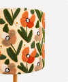 Close-up of a textured lampshade featuring a raised floral pattern with orange, beige, and green flowers on a cream background, mounted on a light wood stem.
