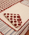A folded white napkin with dark red polka dots and a scalloped edge, placed on a matching tablecloth with blue stripes.